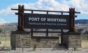 This is a picture of a green train pulling cars down a track at the Port of Montana railroad facility.