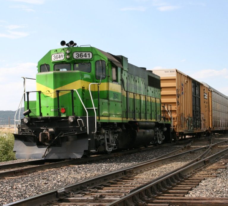 This is a picture of a green train pulling cars down a track at the Port of Montana railroad facility.